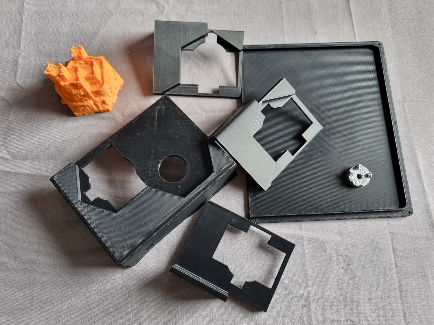 A discarded pile of test prints: various hex cutouts, the Pale Burg fortress in its original orange PLA, and half a backplate that wasn't big enough. A discarded pile of test prints: various hex cutouts, the Pale Burg fortress in its original orange PLA, and half a backplate that wasn't big enough.